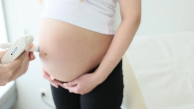 Hand holds doppler device against standing pregnant belly