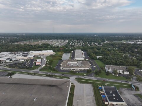 Aerial view of industrial warehouses and office buildings surrounded by green spaces, parking lots, and a small pond in Indianapolis, Indiana, United States.