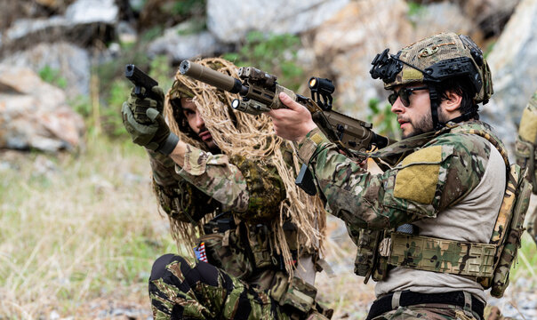 Group of soldiers practicing shooting with rifles and handguns during military training exercises in a rocky outdoor area