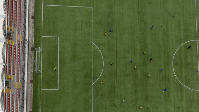 Aerial view of a soccer match in progress on a green pitch with players in colorful jerseys and stadium seating visible in Lagos, Lagos, Nigeria.
