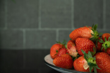 Fresh strawberries on a plate against a black countertop, highlighting vitamin-rich fruit available during the winter season. © Ann