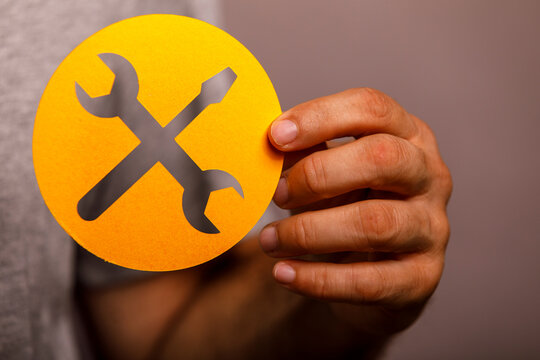 Hand holding a yellow circular icon representing settings, service, or technical support.