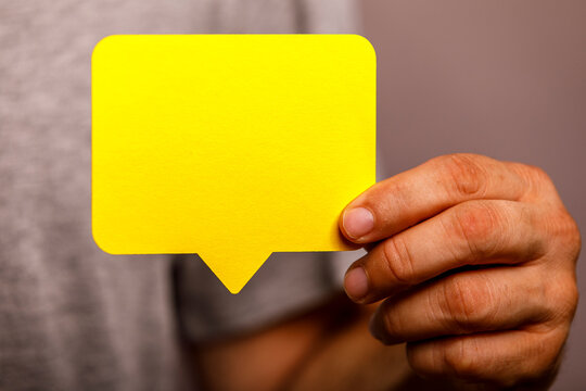 A hand holds a bright yellow blank speech bubble, perfect for your message or idea.