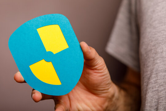 Close-up of a hand holding a shield with a radiation warning sign, symbolizing protection.