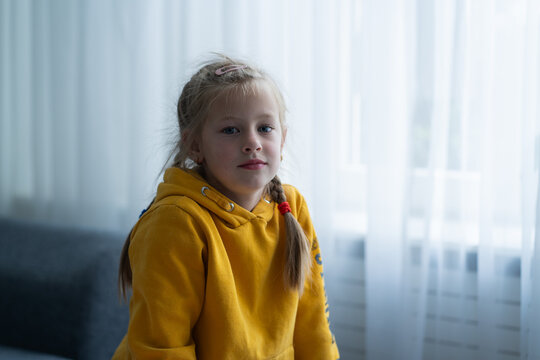 A girl sits on a sofa at home looking calmly into the camera, reflecting a mentally stable and secure state in a family setting. Child psychology articles, parenting resources, mental health