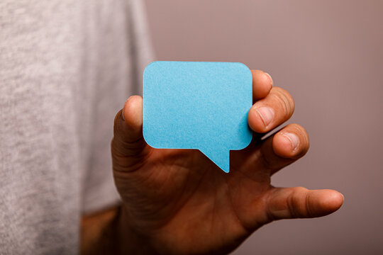 A person's hand holds a blank blue speech bubble, representing communication or ideas.