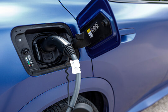 Close-up of a blue electric vehicle (EV) charging, with the power cable plugged into the car's port.