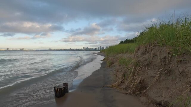 Eroded sandy shoreline and dune grass at Hanlan's Point Beach on the Toronto Islands as gentle Lake Ontario waves reach the narrowing beach.