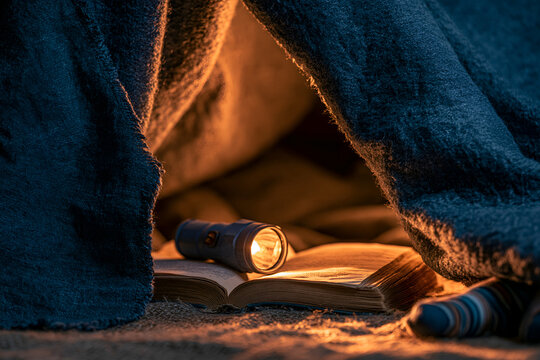 Torch lying on an open book inside a blanket den at bedtime
