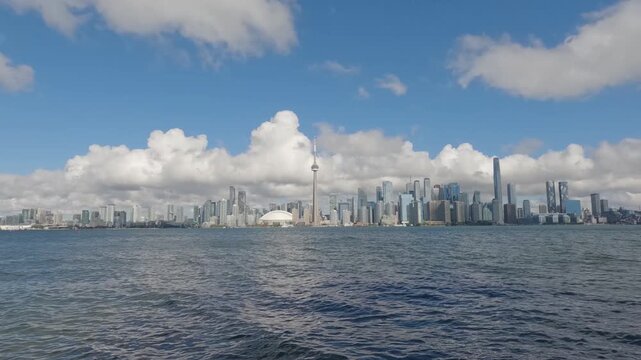 Wide timelapse of Toronto skyline from Centre Island as clouds sweep across the city and a ferry approaches over Lake Ontario.