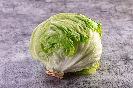 Fresh green iceberg lettuce head on textured gray stone surface, crisp leaves and natural lighting