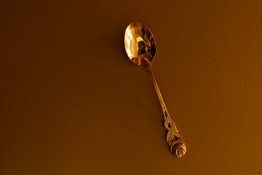 A beautifully crafted golden spoon with an intricate rose design rests on a warm brown surface.