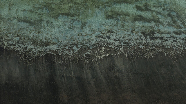 Aerial view of turquoise shallow water meeting dark, textured sand patterns along the coastline in Denham, Western Australia, Australia.