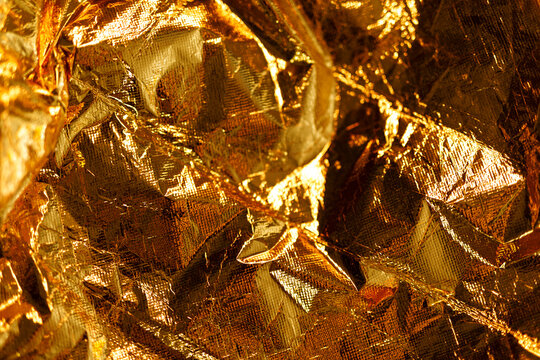 Abstract background featuring shiny, crinkled gold foil with rich texture and reflections.