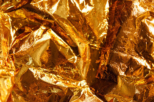 Close-up of shiny, crumpled gold foil creating an abstract textured background.