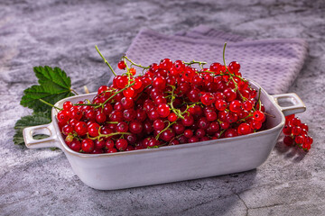 Fresh red currants in white ceramic dish on textured gray surface with green leaf and purple cloth background © Andrei Starostin