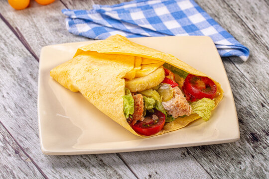 Chicken and hashbrown tortilla wrap with lettuce and tomato on square plate, rustic wood background with blue checkered napkin