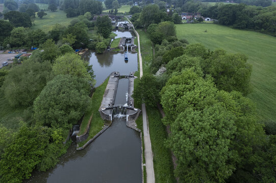 Aerial view of Hatton Locks on the Grand Union Canal, featuring historic canal locks surrounded by lush green fields, trees, and a narrow towpath in Hatton, England, United Kingdom.