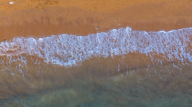Aerial view of golden sand and white sea foam waves washing onto the shore at West Bay, England, United Kingdom.
