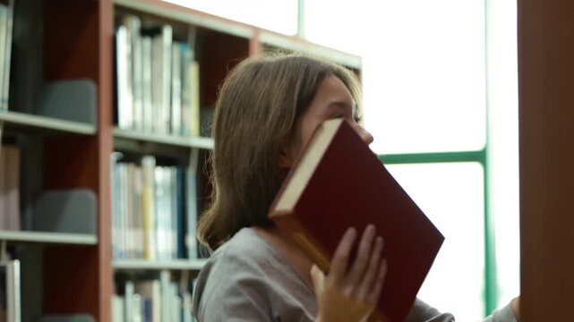 Caucasian teenage girl smiles softly in library. She wears light green headphones and a gray sweater. Background shows blurred rows of book shelves. Education, Back to school
