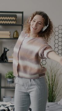 Slow motion of joyful girl with headphones dancing and listening to music spending time in bedroom at home. Entertainment and people concept.