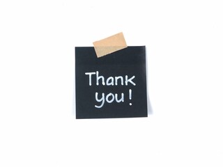 Thank you text handwritten on black adhesive note taped to white background with a piece of beige craft tape. Ideal for expressing gratitude, customer appreciation, and greeting card designs © Eka