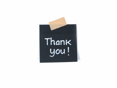 Thank you text handwritten on black adhesive note taped to white background with a piece of beige craft tape. Ideal for expressing gratitude, customer appreciation, and greeting card designs