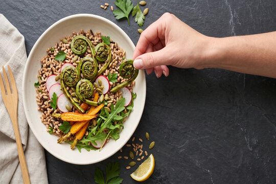 Bowl of ancient grains with fiddleheads and radishes during natural daylight