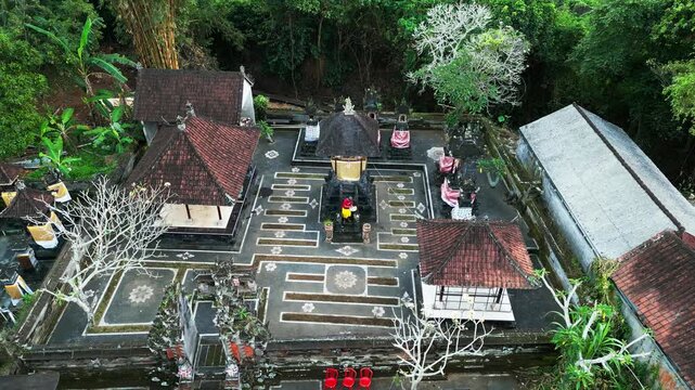 Local worshipper performing daily prayer rituals inside traditional Balinese temple surrounded by dense tropical forest foliage on sacred grounds in Bali orbit aerial drone footage