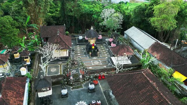 Traditional Balinese temple ceremony with person presenting offering among sacred shrines inside temple courtyard and tropical greenery showcasing Hindu culture push-in aerial drone footage