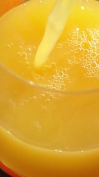 Macro close-up video showing fresh orange juice pouring into a clean transparent glass and forming sparkling fizzy bubbles under bright morning sunlight, perfect for summer refreshment and natural vit