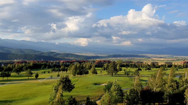 Scenic Golf Course Landscape with Rolling Greens, Trees and Distant Mountains Under Dramatic Clouds
