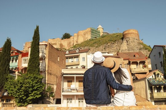 Couple of tourists in street hug enjoy beautiful Tbilisi old city colorful buildings at holidays in Georgia, caucasus. Romantic couple get away together on summer vacation .People and holidays concept