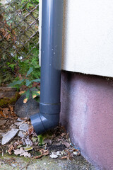 Obraz premium Black rainwater downspout with elbow fitting beside a residential building, exterior drainage pipe connected to house gutter system
