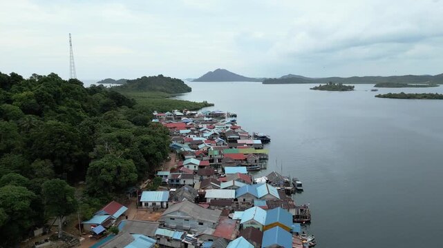 Aerial view of a coastal village with colorful stilt houses nestled between dense forest and the calm sea on Batam Island, Batam, Riau Islands, Indonesia.
