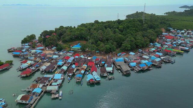 Aerial view of a traditional stilt village with colorful rooftops nestled along the lush coastline of Batam Island in Batam, Riau Islands, Indonesia.