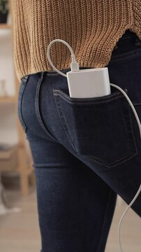 Woman taking a power bank with cable from pants pocket to charge a mobile phone. portable technology, mobile devices and everyday digital convenience.