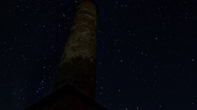 Time lapse of a dark starry night sky with falling meteors and Perseids activity. Celestial lights of sparkling stars and glowing cosmic trails create a dynamic cosmic scene with silhouettes of tower