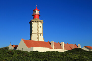 Portugal, Sesimbra. The emblematic, historic lighthouse at Cape Espichel, built in 1870 stands on a huge cliff on the Portuguese West Coast. Clear blue sky - Copy space. © john copland