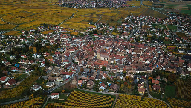 Aerial view of the historic village of Eguisheim with concentric circular streets, colorful half-timbered houses, and surrounding golden autumn vineyards Eguisheim, Grand Est, France.