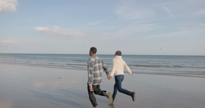 Senior Couple Running Hand in Hand by the Sea