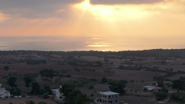 Aerial view of sunset over the coastal landscape with scattered buildings and trees in Famagusta, Famagusta, Northern Cyprus.