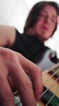 Vertical tight macro perspective focusing on bass strings and fingers pressing frets in dim lighting.