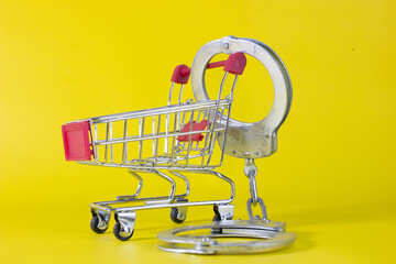 a shopping cart with handcuffs, symbolizing shoplifting, theft, fraud, embezzlement, inventory loss, retail crime, financial investigation, and auditing. © bizdof photo