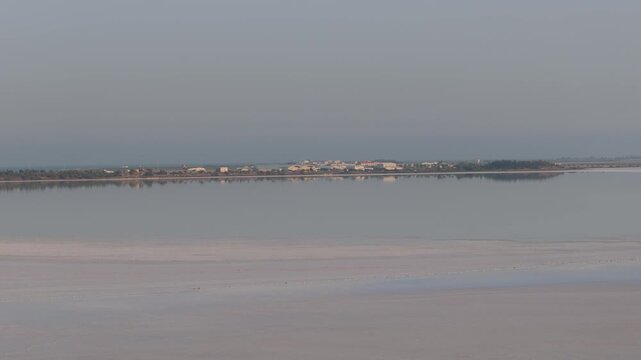 Aerial view of Larnaca Salt Lake with calm water reflecting the distant buildings and horizon in Larnaca, Larnaca, Cyprus.