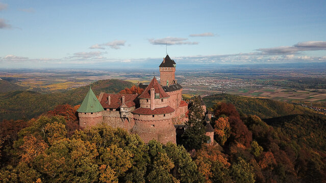 Aerial view of Chateau du Haut-Koenigsbourg surrounded by autumn-colored forests and rolling hills under a clear blue sky in Orschwiller, Grand Est, France.