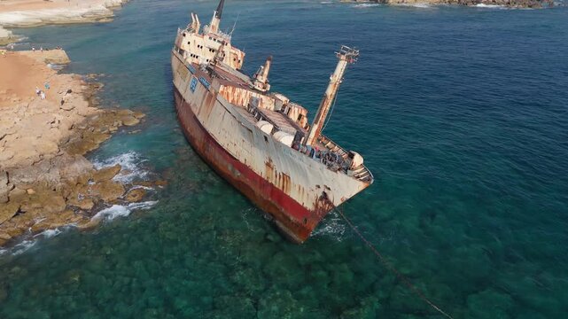 Aerial view of the rusted Edro III shipwreck grounded on the rocky coastline with clear turquoise water in Peyia, Paphos, Cyprus.