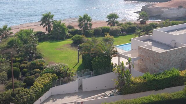 Aerial view of a coastal villa with a swimming pool, lush gardens, and palm trees overlooking the sea in Nicosia, Nicosia, Cyprus.