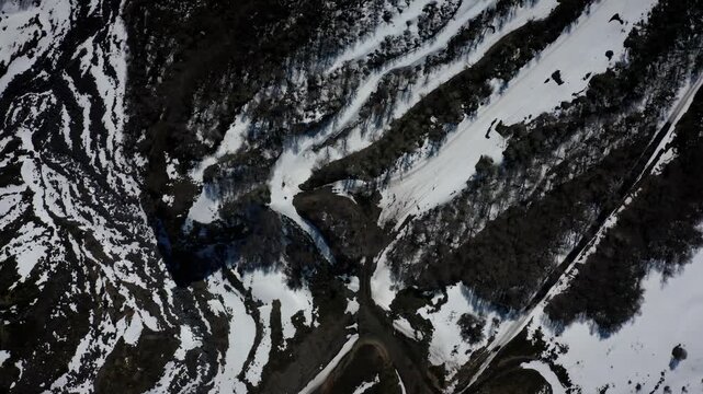 Top down aerial view of snowy mountain terrain and a winding road