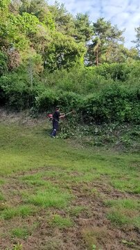 Man Trimming Overgrown Grass and Brush with String Trimmer Outdoors
